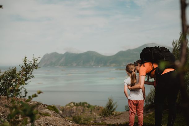 Familiefoto fra en fjelltur hvor ei jente står på toppen av et fjell